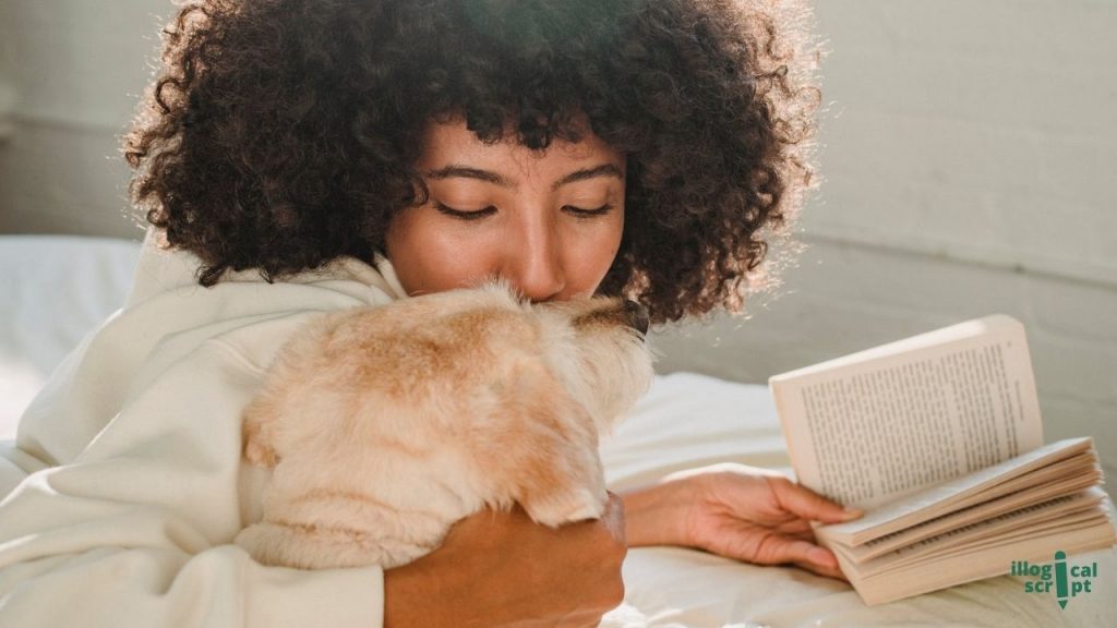 a woman ling on bed with a book in one hand and cuddling a dog with other