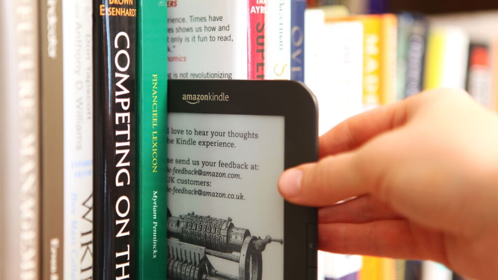 kindle among stacks of books | Kindle vs. Audible