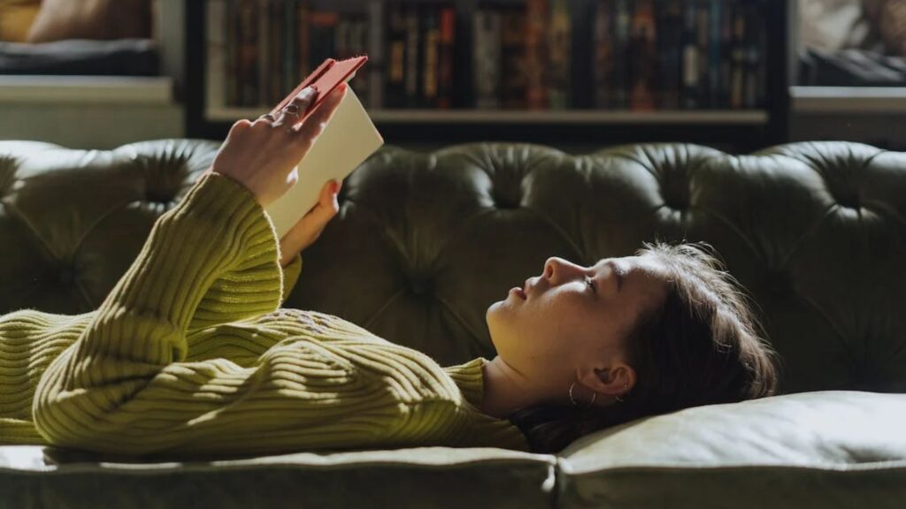 women in olive sweater lying on the couch and reading