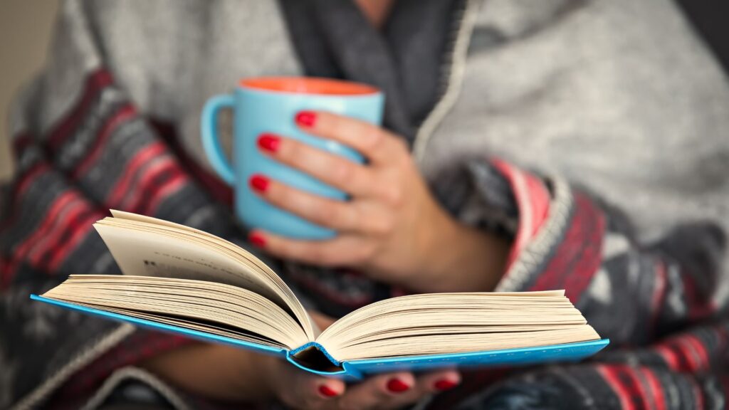 A women reading book and holding cup in another hand.  | Advantages and Disadvantages of Silent reading